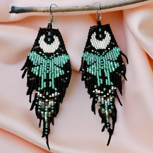 Handmade beaded earrings with a moon and turquoise butterfly design, featuring a black fringe. The earrings are hung from hypoallergenic 316L surgical steel lever backs.