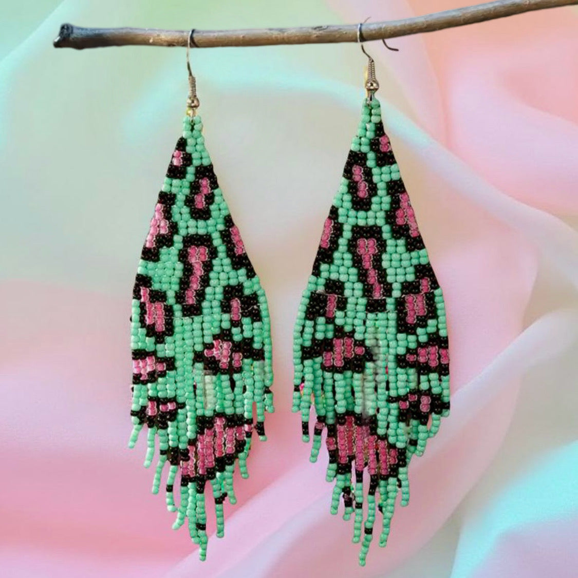 Handmade beaded earrings with green and pink leopard print design, featuring fringe detail and hypoallergenic 316L surgical steel lever backs, displayed against a pastel background.