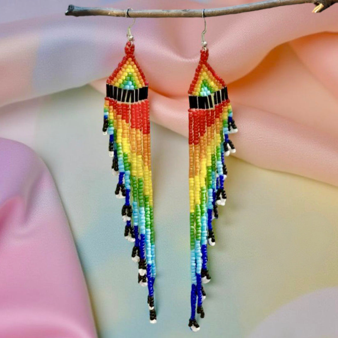 Long handmade beaded earrings with a vibrant rainbow fringe, displayed against a pastel background on a wooden hanger.