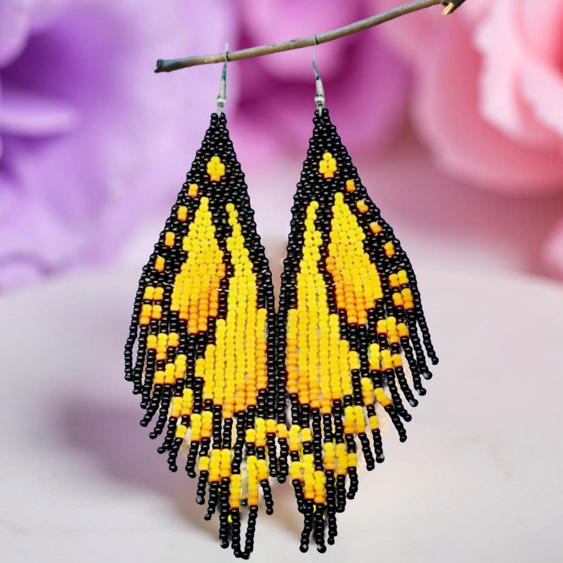 Handmade beaded earrings designed to resemble yellow butterfly wings with black accents, displayed against a floral background.