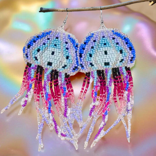 Handmade beaded jellyfish earrings in blue, purple, and pink with delicate flowing tentacles, featuring hypoallergenic surgical steel lever back hooks. Pearlescent background