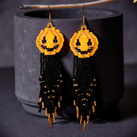 Handmade Halloween beaded earrings with yellow smiley pumpkin faces and long black and gold beaded fringe hanging from hook-style ear wires.