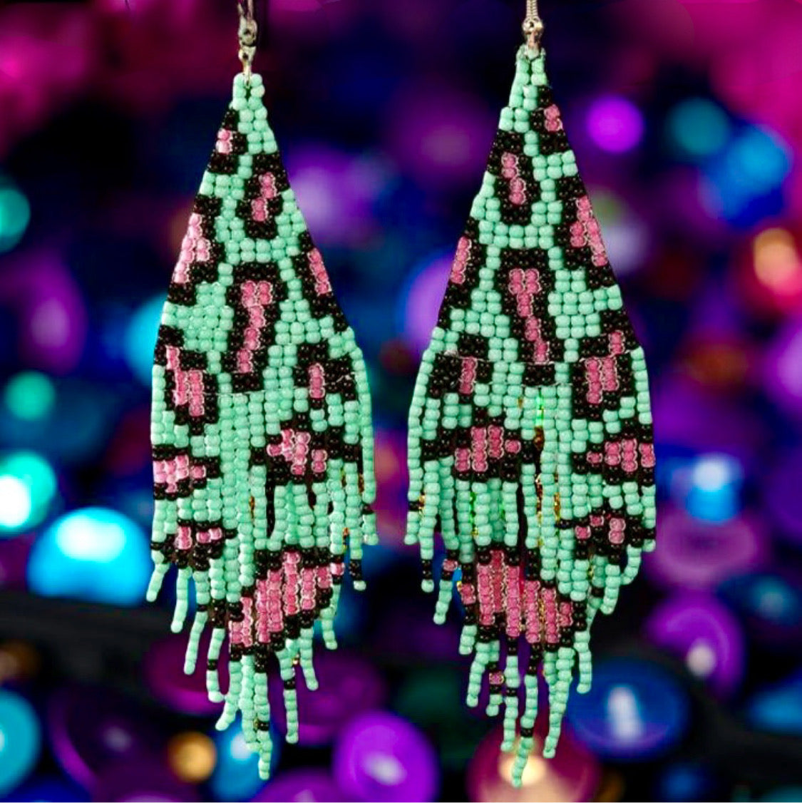 Handmade beaded earrings with green and pink leopard print design, featuring fringe detail and hypoallergenic 316L surgical steel lever backs, displayed against a sequin background.