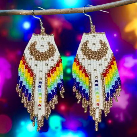 Handmade beaded earrings with a moon design, white and rainbow-colored fringe, and hypoallergenic medical-grade 316L surgical steel lever backs, set against a cosmic purple backdrop.