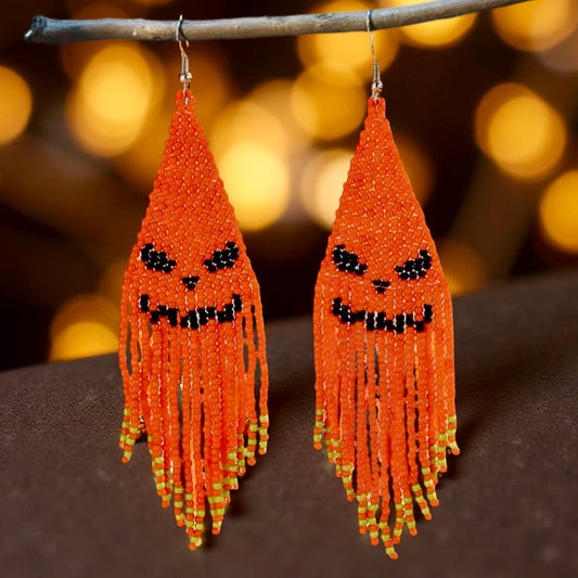 Handmade beaded earrings with an orange jack-o'-lantern face design and long orange fringe, perfect for Halloween-themed outfits.