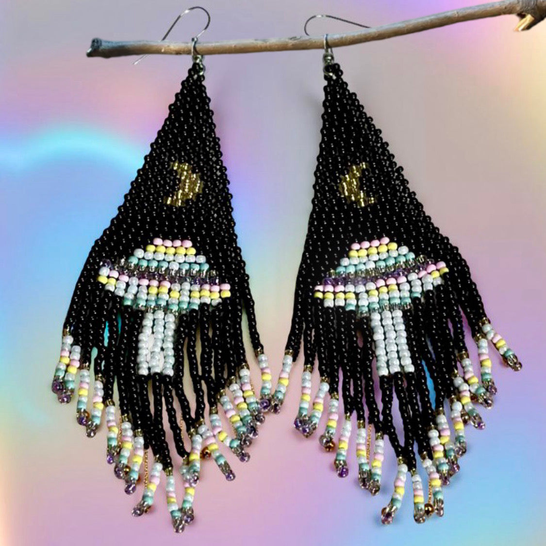 Handmade beaded earrings with black fringe, featuring a UFO and moon design. The earrings are mounted on surgical steel lever backs and show intricate bead detailing.
