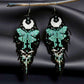 Handmade beaded earrings with a moon and turquoise butterfly design, featuring a black fringe. The earrings are hung from hypoallergenic 316L surgical steel lever backs. Black satin background 