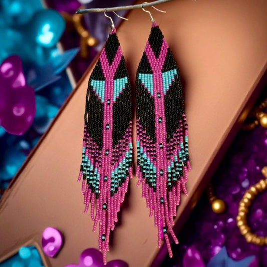 Close-up image of handmade beaded earrings with black, pink, and blue fringe, hanging on 316L surgical steel lever back hooks.