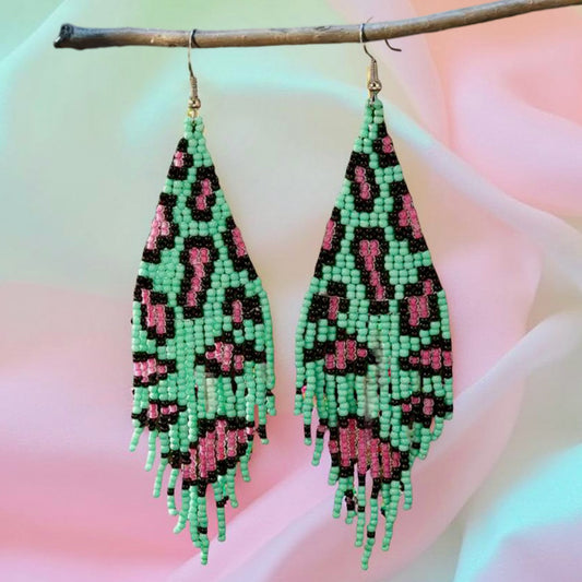 Handmade beaded earrings with green and pink leopard print design, featuring fringe detail and hypoallergenic 316L surgical steel lever backs, displayed against a pastel background.