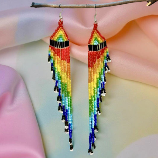 Long handmade beaded earrings with a vibrant rainbow fringe, displayed against a pastel background on a wooden hanger.