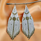 Handmade beaded earrings with a white and gold moon phase design, hanging from a twig against a soft satin background.