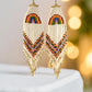 Handmade beaded earrings with a rainbow design at the top and long fringe, featuring colourful beads in red, yellow, green, blue, and purple. The earrings are finished with hypoallergenic 316L surgical steel lever backs.