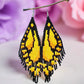Handmade beaded earrings designed to resemble yellow butterfly wings with black accents, displayed against a floral background.