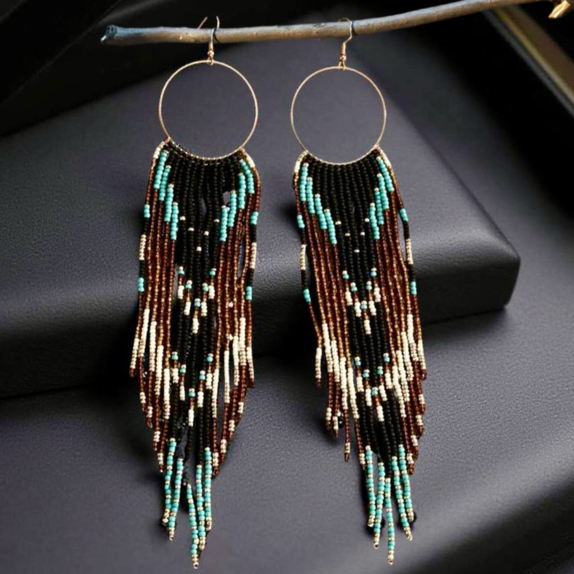 Handmade beaded earrings featuring a hoop and long fringe, with turquoise, brown, black, and cream beads. The earrings are finished with hypoallergenic 316L surgical steel lever backs.