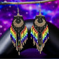 Handmade beaded earrings with a moon design, black and rainbow-coloured fringe, and hypoallergenic medical-grade 316L surgical steel lever backs, set against a cosmic purple backdrop.