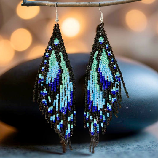 Handmade beaded earrings featuring a blue butterfly wing fringe, with intricate beadwork in shades of turquoise and blue. The earrings are attached to hypoallergenic 316L surgical steel lever backs.