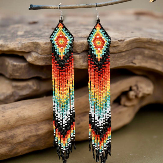 Handmade beaded earrings featuring a long fringe design with a vibrant colour palette of orange, red, yellow, turquoise, black, and white. The earrings have hypoallergenic 316L surgical steel lever backs.