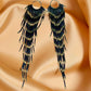 Handmade beaded earrings with extra-long black and gold fringe displayed on a soft beige satin background.