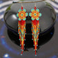 Handmade beaded earrings featuring a flower design with red, orange, yellow, and turquoise beads, complemented by long tassel fringe, with hypoallergenic 316L surgical steel lever backs