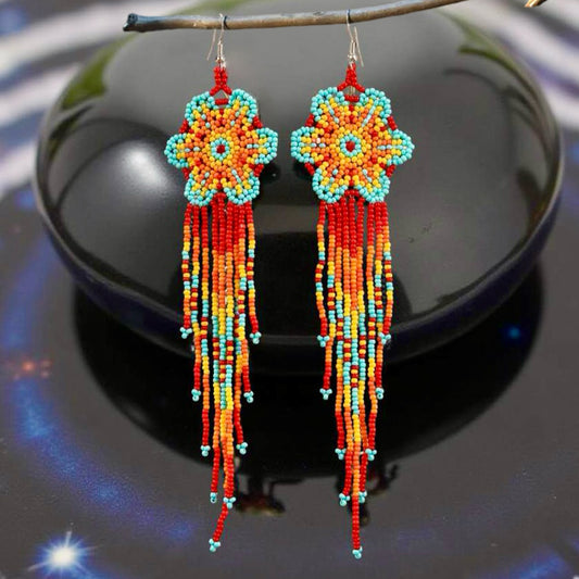 Handmade beaded earrings featuring a flower design with red, orange, yellow, and turquoise beads, complemented by long tassel fringe, with hypoallergenic 316L surgical steel lever backs