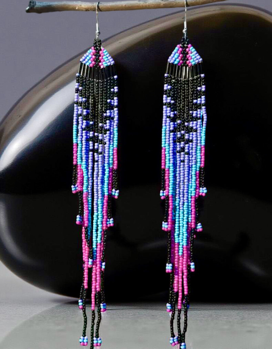 Long beaded earrings with colourful seed beads imitating a jellyfish in front of a shiny black surface