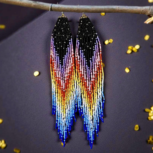 Handmade beaded earrings with a long rainbow fringe, transitioning from black to purple, pink, red, yellow, and blue, hanging from hypoallergenic 316L surgical steel lever backs.
