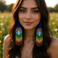 Beautiful woman wearing handmade beaded earrings with a colorful rainbow fringe and red-and-white mushroom design, finished with hypoallergenic surgical steel hooks.