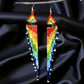 Long handmade beaded earrings with a vibrant rainbow fringe, displayed against a black satin background on a wooden hanger.