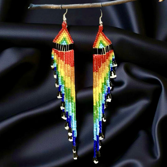 Long handmade beaded earrings with a vibrant rainbow fringe, displayed against a black satin background on a wooden hanger.