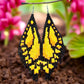 Handmade beaded earrings designed to resemble yellow butterfly wings with black accents, displayed against a garden background.