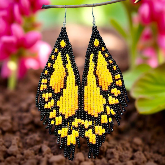 Handmade beaded earrings designed to resemble yellow butterfly wings with black accents, displayed against a garden background.