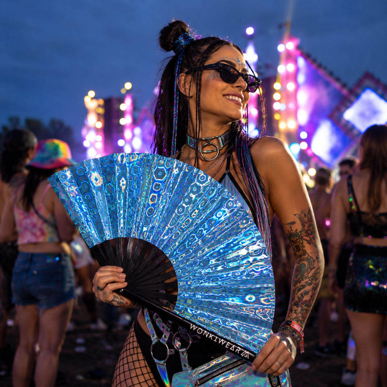 Festival attendee using blue holographic fan at outdoor music festival