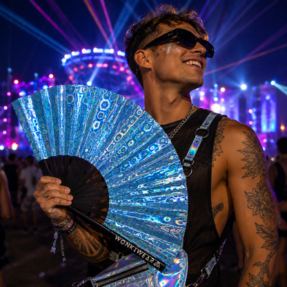 Male festivalgoer holding blue holographic rave fan at music festival