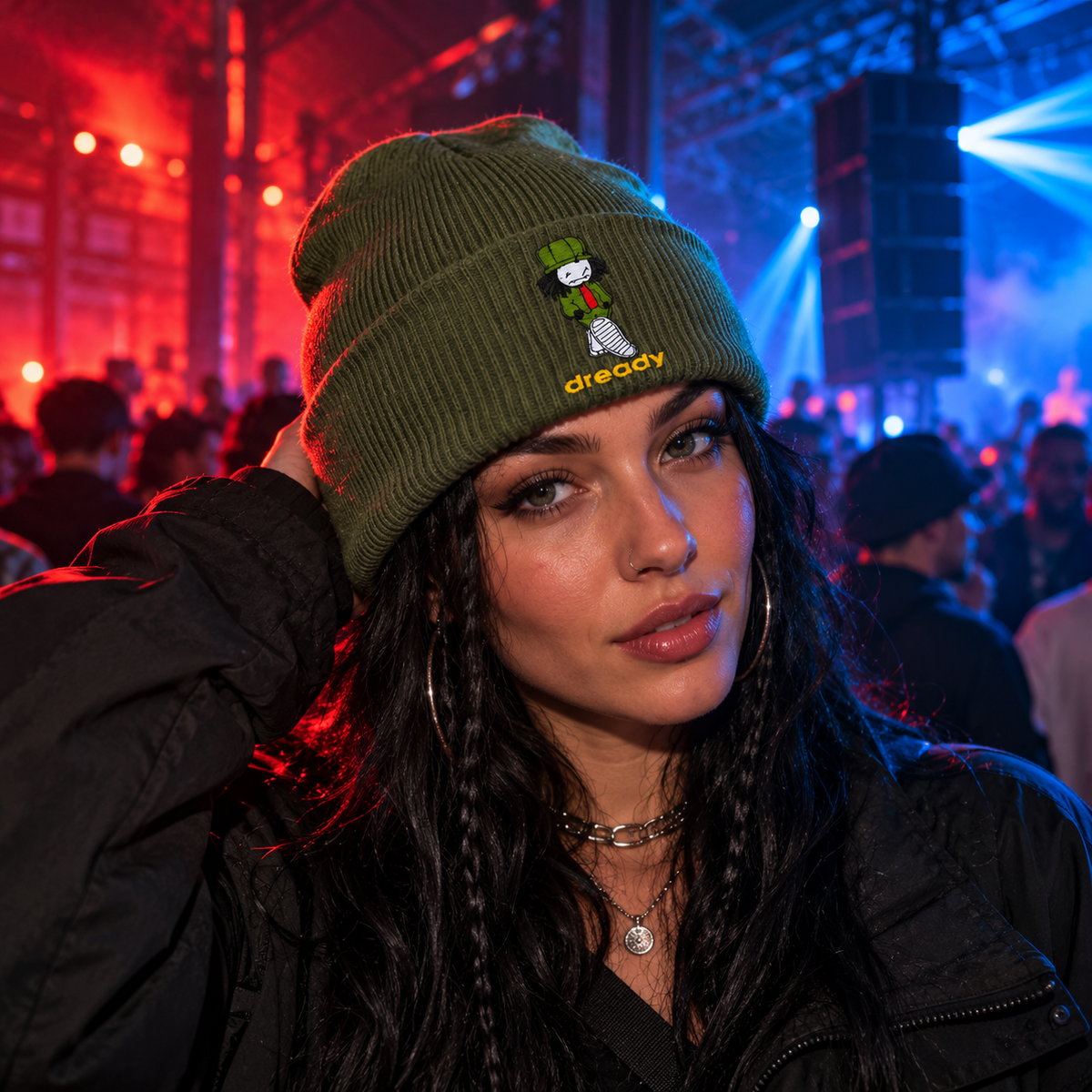Model wearing the olive green Dready Walking Man embroidered beanie at a drum and bass rave, styled with alternative streetwear under red and blue club lighting.