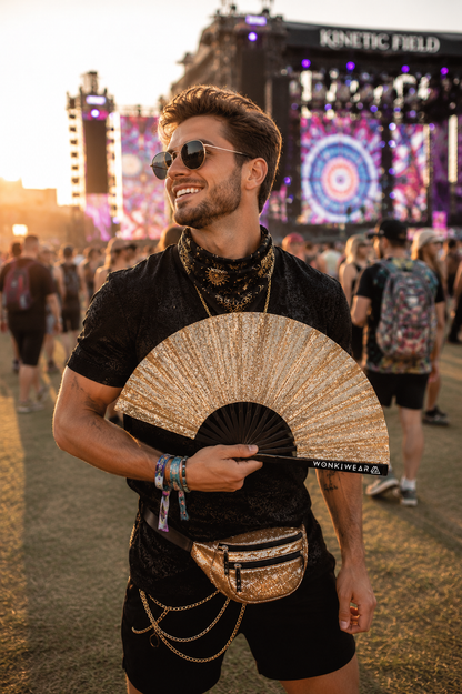 Male festival model holding gold glitter rave fan at outdoor music festival