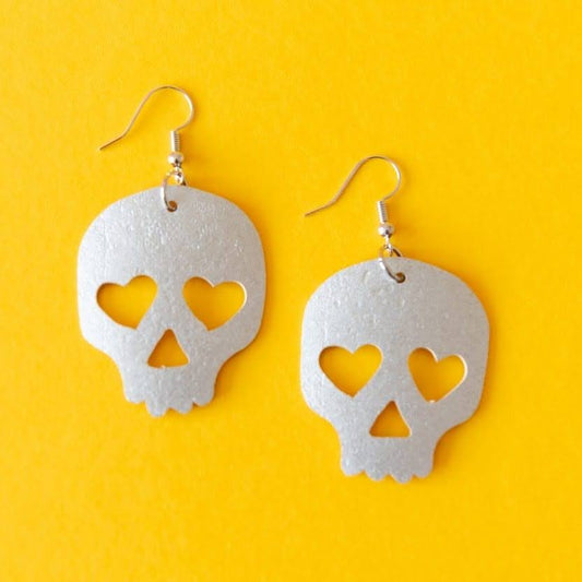 Trend Tonic gold or silver skull drop earrings with heart-shaped eye cut-outs, product view.