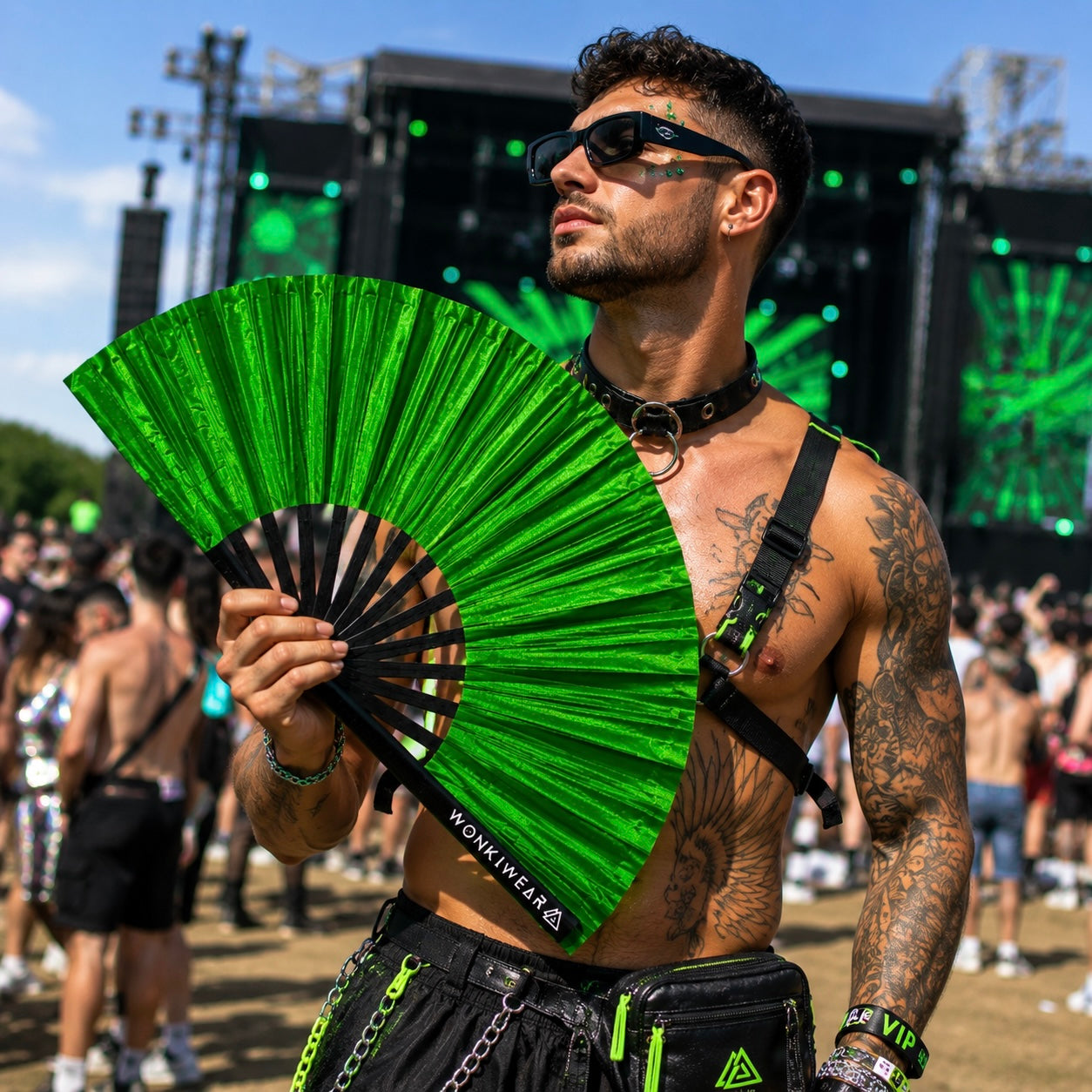 Male festival goer holding XL green shimmer festival fan at summer event