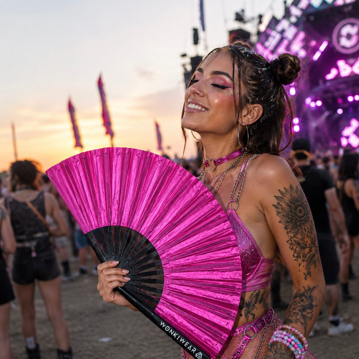 Festival attendee using hot pink shimmer festival fan at outdoor music festival