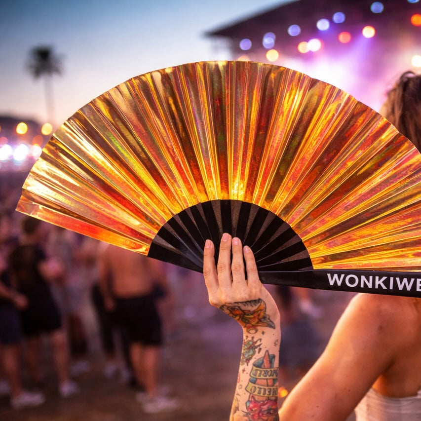 Person holding iridescent festival fan at sunset rave with glowing orange lighting