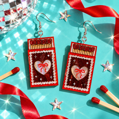 Matchbook earrings with glittery red match heads and pearlescent heart details by Cuteryko