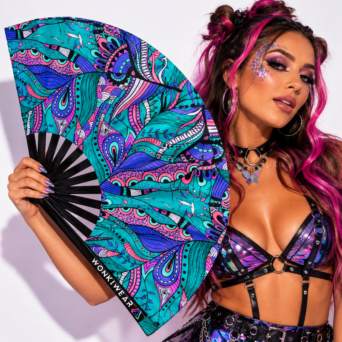 Model posing in a holographic rave outfit with the WonkiWear Mystic Paisley XL folding fan, featuring vibrant teal, purple and pink paisley artwork with black ribs.