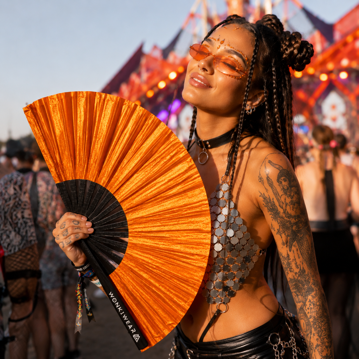 Festival goer using orange shimmer festival fan outdoors at a music festival