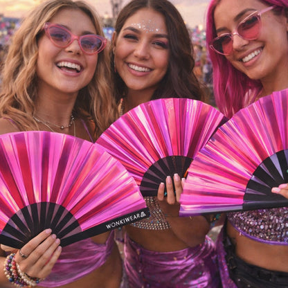 Group of women holding pink iridescent festival fans at a rave wearing colourful outfits