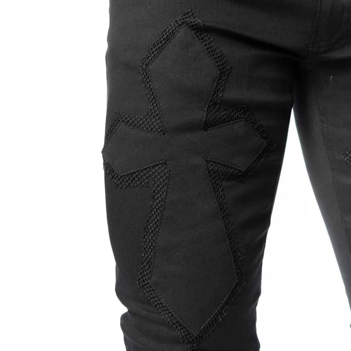 Close-up of embroidered cross detailing on the thigh of black gothic trousers