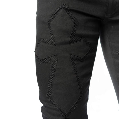 Close-up of embroidered cross detailing on the thigh of black gothic trousers