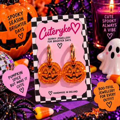 Glittery translucent pumpkin hoop earrings with jack-o-lantern charms on Halloween background