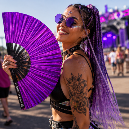 Festival attendee using purple shimmer festival fan at outdoor music festival