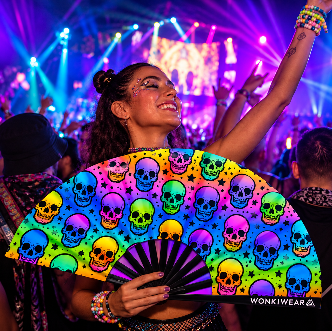 Rainbow skull XL festival fan with black ribs held by a woman in a colourful neon rave crowd