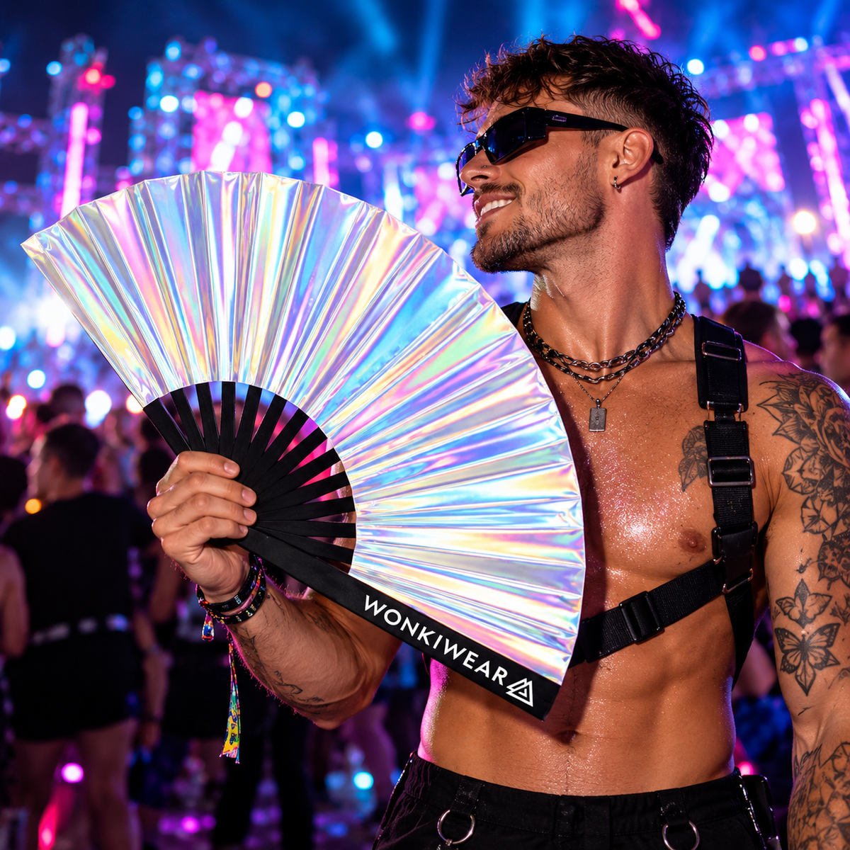 Silver stardust iridescent rave fan with WonkiWear branding held by a male festival-goer under neon lights