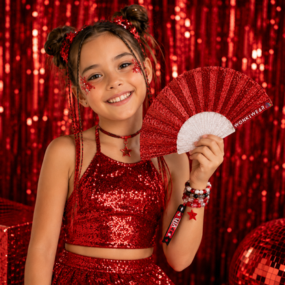 Child holding red glitter folding fan at outdoor event
